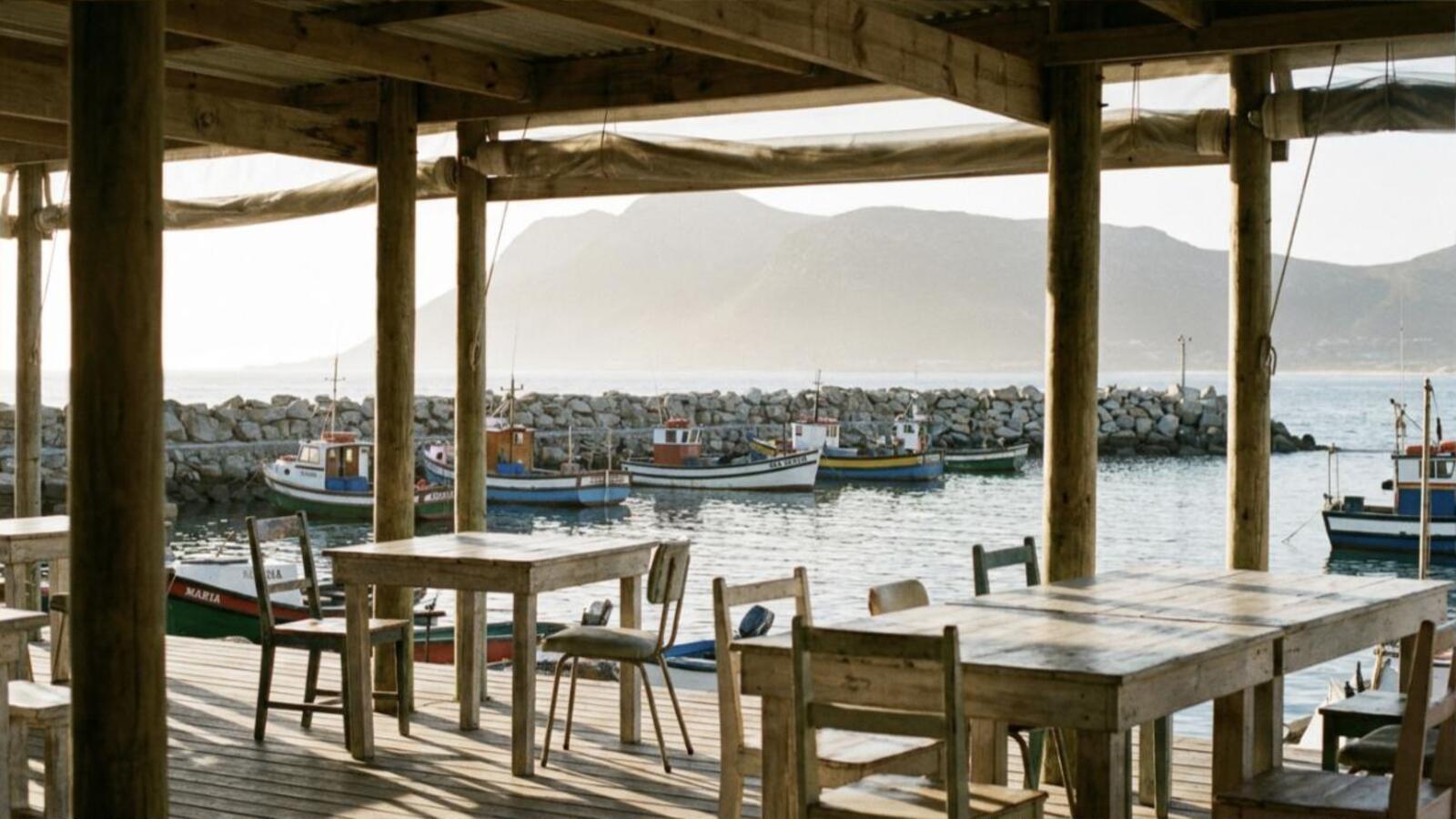 The covered deck at Slipway Kitchen looking out over the fishing boats in the Gordon's Bay old harbour at golden hour.